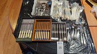 Overview of four groupings: two boxes of steak knives at front, assorted flatware in trays behind
