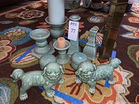 Two foo dog porcelain figurines and multiple green porcelain candlesticks and vases shown on a multicolored patterned rug.