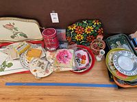 Wide view showing the variety of serving trays, plates, napkin holders, coffee tin, and napkins arranged together on a surface.