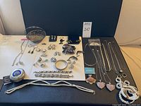 Full overview of assorted necklaces, bracelets, rings, brooches, earrings, trinket dish, enamel box, keychain on black surface