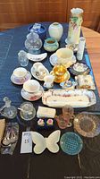 Full view of the lot items on a black cloth displaying various bowls, vases, teacups, dishes, and crystal piano figurine.