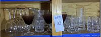 Shelf with assorted glassware including red stemmed glasses, clear wine glasses, and tumblers.