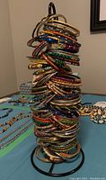 Full view of black metal stand with approximately 100 colorful bangles stacked in varied materials and designs, bangles measure about 2.5 diameter.