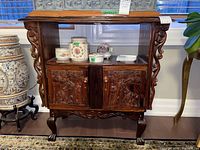 Wooden cabinet with carved giraffe and floral details on doors and sides, displayed with decorative items on top.