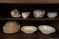 Full view of multiple sets of plates, teacups with saucers, stacked and arranged on shelves.