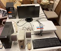 Full setup of Acer desktop computer with keyboard, mouse, speakers, Asus monitor, HP printer, power bar, Nokia flip phone, Samsung smartphone and blank CDs on table