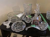 Collection of various crystal and glass items including vases, dishes, a pipe-shaped dish, and small bowls placed on a black surface.