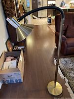 Full view of floor lamp showing flexible gooseneck arm, conical brushed brass shade, and slender brass pole with weighted base.