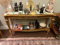 Full frontal view of the gold-colored wood hall table with various items on top and shelf, showing overall structure and design.