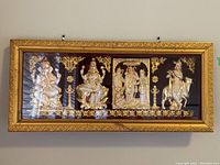 Full view of the shadow box with four gold Hindu deity figures inside an ornate golden frame hung on a wall.