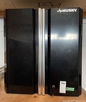 Closed black Husky metal cabinet with two chrome-like handles and lock with two keys attached.