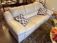 Front-side view of beige/light gray leather three-seater sofa with two patterned throw cushions.