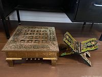Wood and metal prayer stool with embossed decorative panels and painted folding book stand positioned on floor.