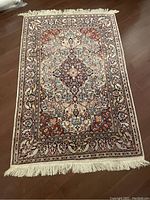 Full view of intricately patterned area rug approximately 4x6 feet, showing central medallion and colorful flowers with fringe on ends.