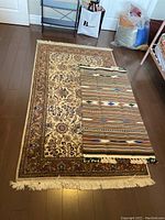 Both rugs displayed on wood floor. Larger floral medallion rug with smaller reversible striped rug partially on top.