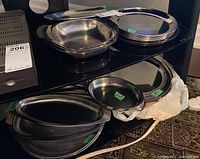 Photo of various sizes of stainless steel serving trays and dishes stacked on shelves, including round plates and oval trays with handles.