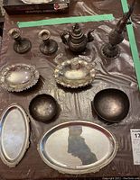 Full view of ten pieces of sterling and metalware service pieces and décor including candleholders, teapot, vases, trays, and bowls laid on table