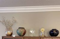 Lot showing three different vases and two clocks displayed on a wooden surface against a neutral wall.