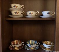 Wooden shelf displaying seven cups and saucers (three coloured sets bottom shelf, four plain sets top shelf)