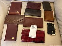 Overview of 11 wallets, coin purses, and notebook holders arranged on a sofa. Various sizes, colors, and styles of brown, burgundy, and black.