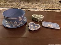 Full lot showing blue jasperware bowl with plate, green heart-shaped lidded box, blue small heart-shaped plate, and rectangular plate with white relief decorations on wood floor