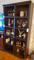 Front view of the wood cubby style bookcase with 10 square cubbies containing decorative figurines, bottles, and mugs, subject to not being included in sale.