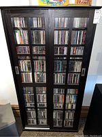 Front view showing full height nine shelves filled with CDs behind sliding glass doors with grid detail.