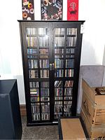 Front view of tall black wooden cabinet with glass doors filled with CDs, showing overall appearance and height.
