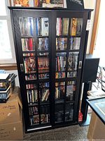 Front view of the black wooden bookcase showing glass sliding doors and media contents inside