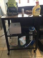 Photo of one black metal frame utility cart with wood top, lower mesh shelves, various items on the cart (not included) and caster wheels.