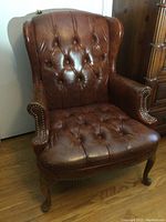 Front view of a brown leather wingback chair with tufted seat and backrest, showing overall condition and style.