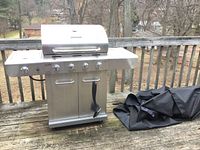 Full view of stainless steel Char-Broil propane grill with cabinet base and side burner, outdoors on wooden deck alongside black grill cover.