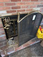 Photo of fireplace screen and toolset on a hearth, showing tools in stand with brick wall background.