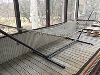 Full side view of rope hammock mounted on black tubular metal stand on wooden deck outdoors.