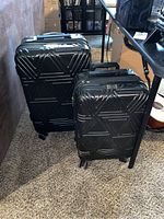 Front view showing two black hard-shell suitcases with geometric pattern on carpet.