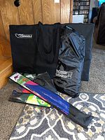 Photo showing GoSports Cornhole and Ladder Toss carrying bags, plus four folded kites in fabric bags arranged on carpeted floor.