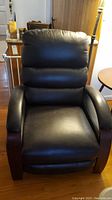 Front view of black bonded leather recliner chair showing padded seat, backrest, and curved wooden arms