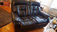 Front view of the black leather double recliner loveseat showing two seats with cushioned backs and armrests.