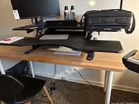 Full side view showing the Varidesk ProPlus 48 black adjustable standing desk on a wooden desk surface with items on top including computer monitor and bag.