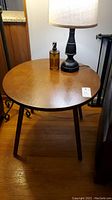 Photo showing round wooden side table with lamp and soap bottle on top, highlighting wood grain and surface condition.