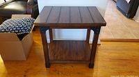 Front view of the wooden side table showing slatted top and lower shelf with metal reinforcements on corners.