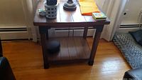 Full view of wooden side table showing its rectangular top with items on it and wooden floor beneath.