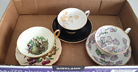Three assorted cups and saucers with floral and fruit patterns, gold accents