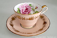Porcelain cup and saucer with pink exterior, gold accents, and pink rose floral design inside the cup.