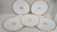 Five white porcelain Minton dinner plates arranged in a circle showing the gold scalloped rims and central gold floral medallions.