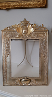 Full view of ornate metal easel frame with detailed border and crest ornament.