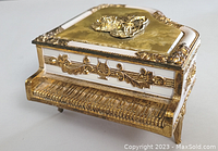 Front angle showing piano keys and gold floral design on music box shaped like a grand piano.
