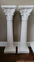 Front view of the pair of white plaster decorative columns showing fluted shafts and ornate Corinthian capitals.