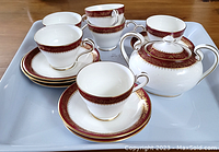 Partial dessert set on white tray featuring 4 teacups, 3 saucers, 3 plates, and sugar bowl with lid