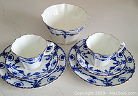 Cups, saucers, and bowl with blue floral and scroll patterns and gold trim.